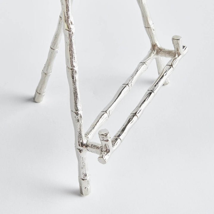 Elevate your decor with this sturdy and resilient silver easel, expertly crafted to exhibit platters, cookbooks, or small art pieces. The traditional aesthetic of bamboo-like silver details adds a timeless charm, while the versatile design allows for effortless display of various items.