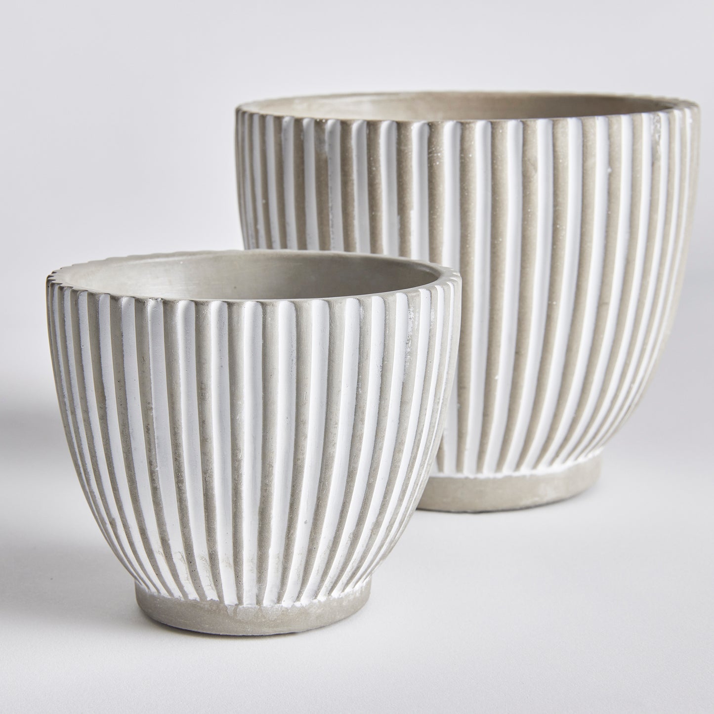 With its modern vertical line pattern and sleek white wash, the Adara Concrete Planter Pots set is perfect for adding an artistic touch to any contemporary space. This set includes two pots, providing you with the perfect opportunity to enhance the aesthetic of your home or office with your favorite flowers or plants. The tapered design of these pots makes them versatile and stylish, suitable for a variety of plants, ensuring all your botanical needs are met.