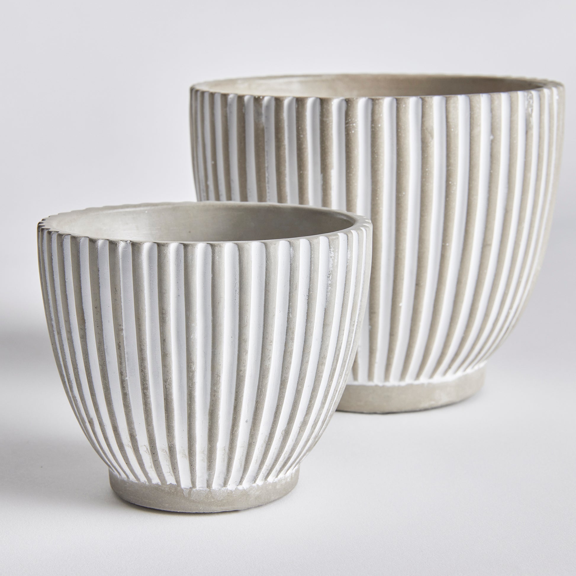 With its modern vertical line pattern and sleek white wash, the Adara Concrete Planter Pots set is perfect for adding an artistic touch to any contemporary space. This set includes two pots, providing you with the perfect opportunity to enhance the aesthetic of your home or office with your favorite flowers or plants. The tapered design of these pots makes them versatile and stylish, suitable for a variety of plants, ensuring all your botanical needs are met.