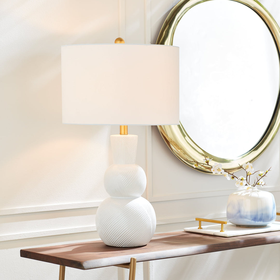 This traditional table lamp is crafted from clean white ceramic and features hand carved markings on the body, making it a perfect addition to any traditional setting. It is complemented by a white linen shade and a simple brass finial. Ideal for enhancing the ambiance of any living room or home decor.