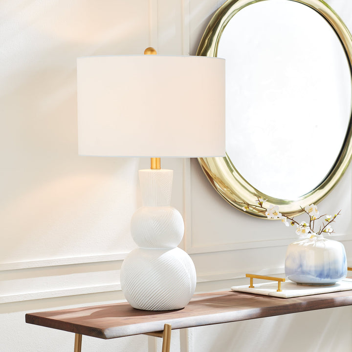 This traditional table lamp is crafted from clean white ceramic and features hand carved markings on the body, making it a perfect addition to any traditional setting. It is complemented by a white linen shade and a simple brass finial. Ideal for enhancing the ambiance of any living room or home decor.