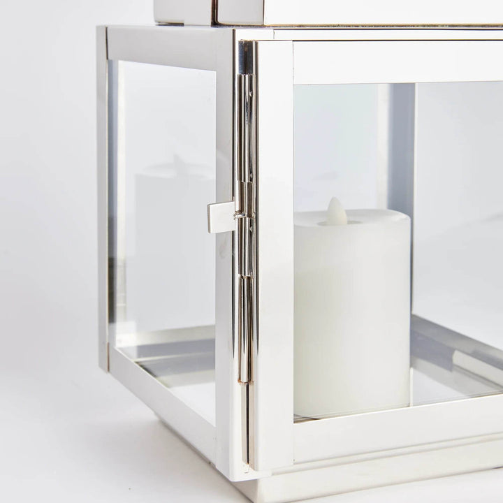 Featuring a teak handle, wide glass panes, and a tailored square profile, this outdoor lantern adds a touch of elegance to your patio, porch, or lanai. Its exclusive chrome design sets it apart from the rest. A beautiful and unique addition to any outdoor space.