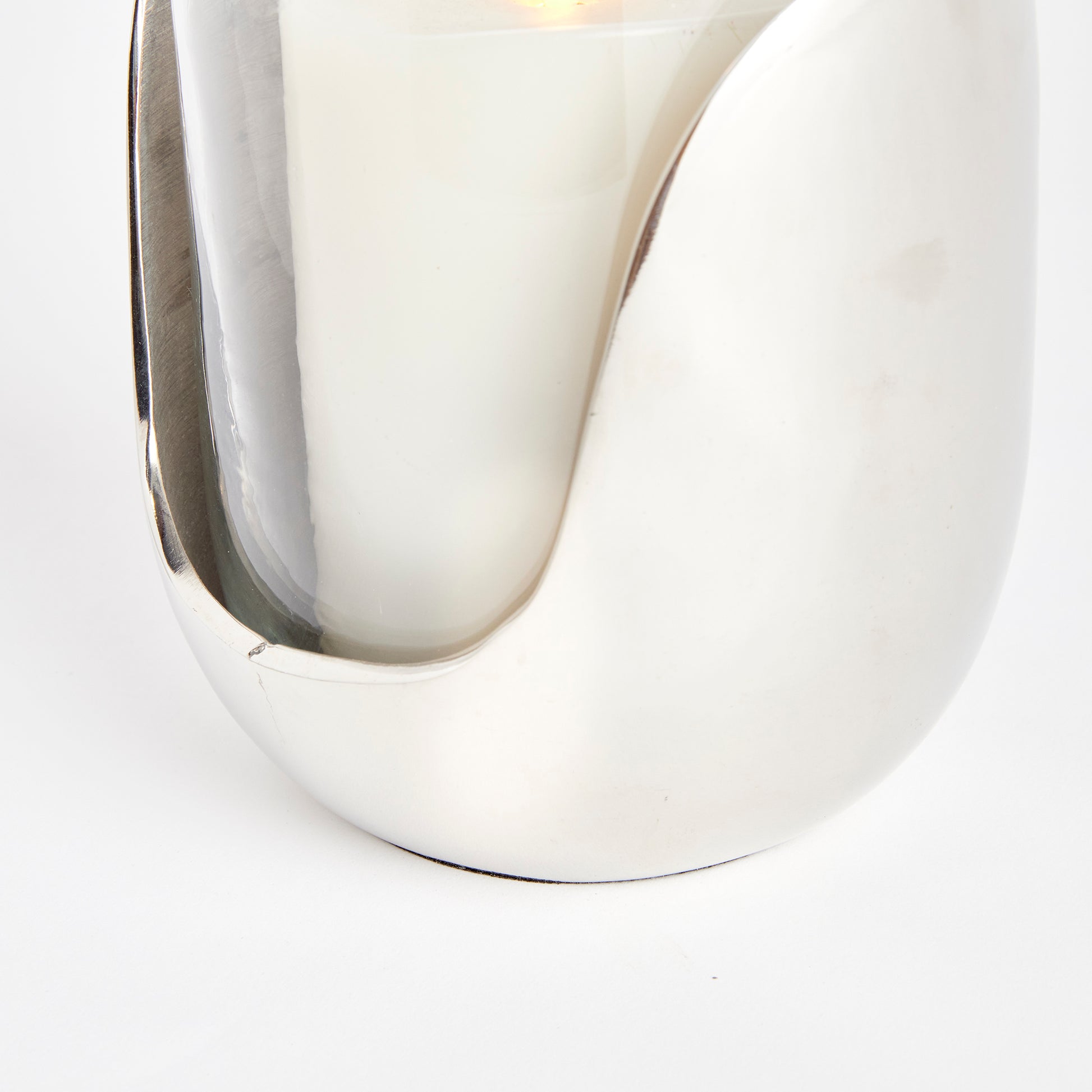 This exquisite hurricane is a beautiful blend of well-planned design and a variety of materials. It showcases hand blown glass that effortlessly fits into an abstract cast aluminum base with a sleek silver finish. Perfect for a side table, console, or mantel, this one-of-a-kind piece adds a touch of contemporary elegance to any space.