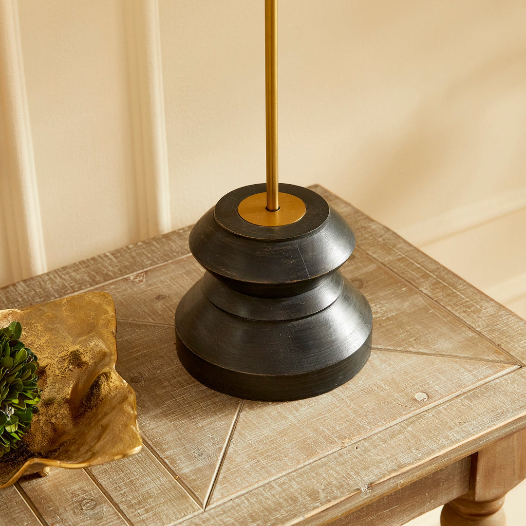 This tall, narrow lamp features a geometric turned wood black wash base, making it ideal for placement on either side of a long console or entry table. With its sleek and straightforward design, it provides a lovely way to illuminate a room with its soft light and black and gold accents, complemented by a linen shade.