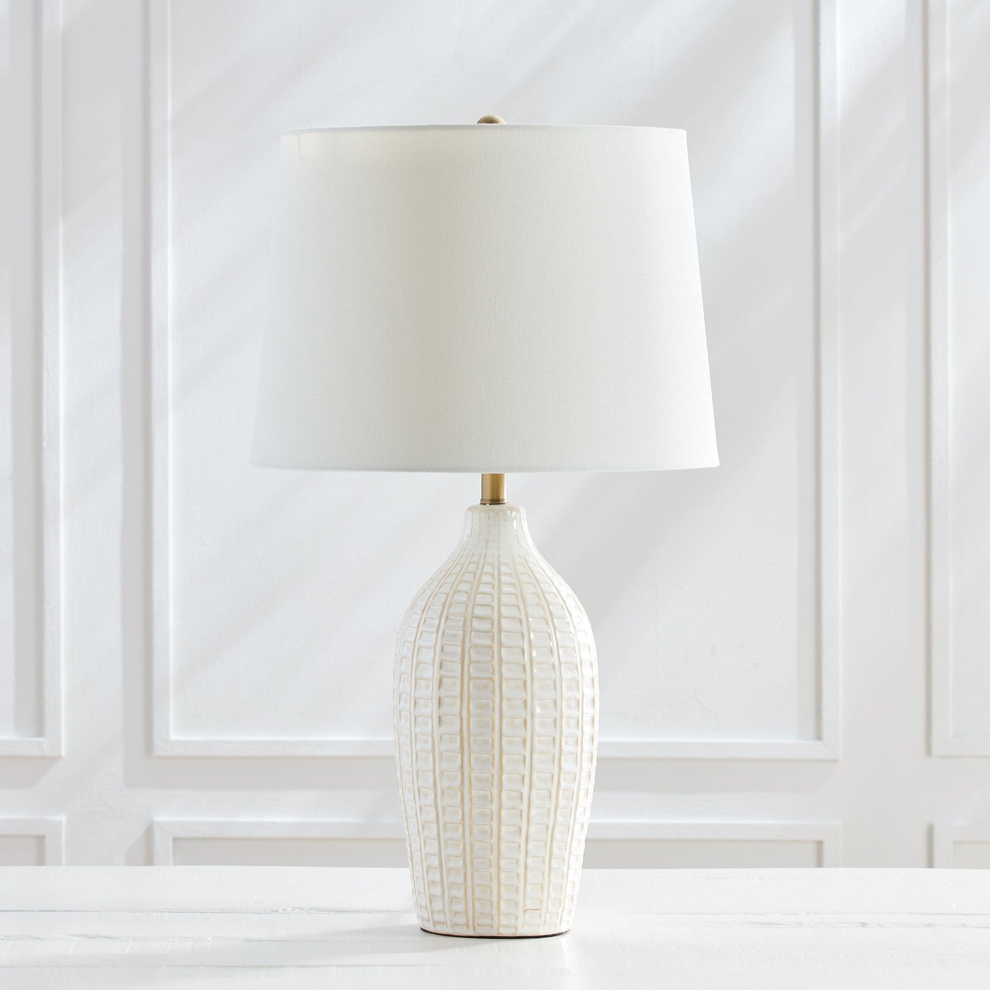 With a pressed pattern on the ceramic body, the Nadia Lamp is a work of art. Topped off with a generously scaled fabric shade, it is sure to enhance any space. intricate details, bold, finial, classic white, metal accents This ceramic lamp boasts an eye-catching pressed pattern and an elegantly designed fabric shade, making it an artistic addition to any room. With intricate details, a bold finial, and classic white coloring with metal accents, it offers both style and subtlety.