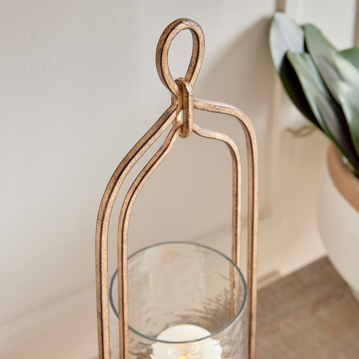 Crafted with precision from sturdy cast aluminum and adorned with exquisite hammered glass, the Amara Gold Hurricane Candle Holder Small showcases a perfect balance of lyrical form and substantial design. A decorative yet functional loop handle completes the look, making it a versatile addition to any transitional or modern setting.