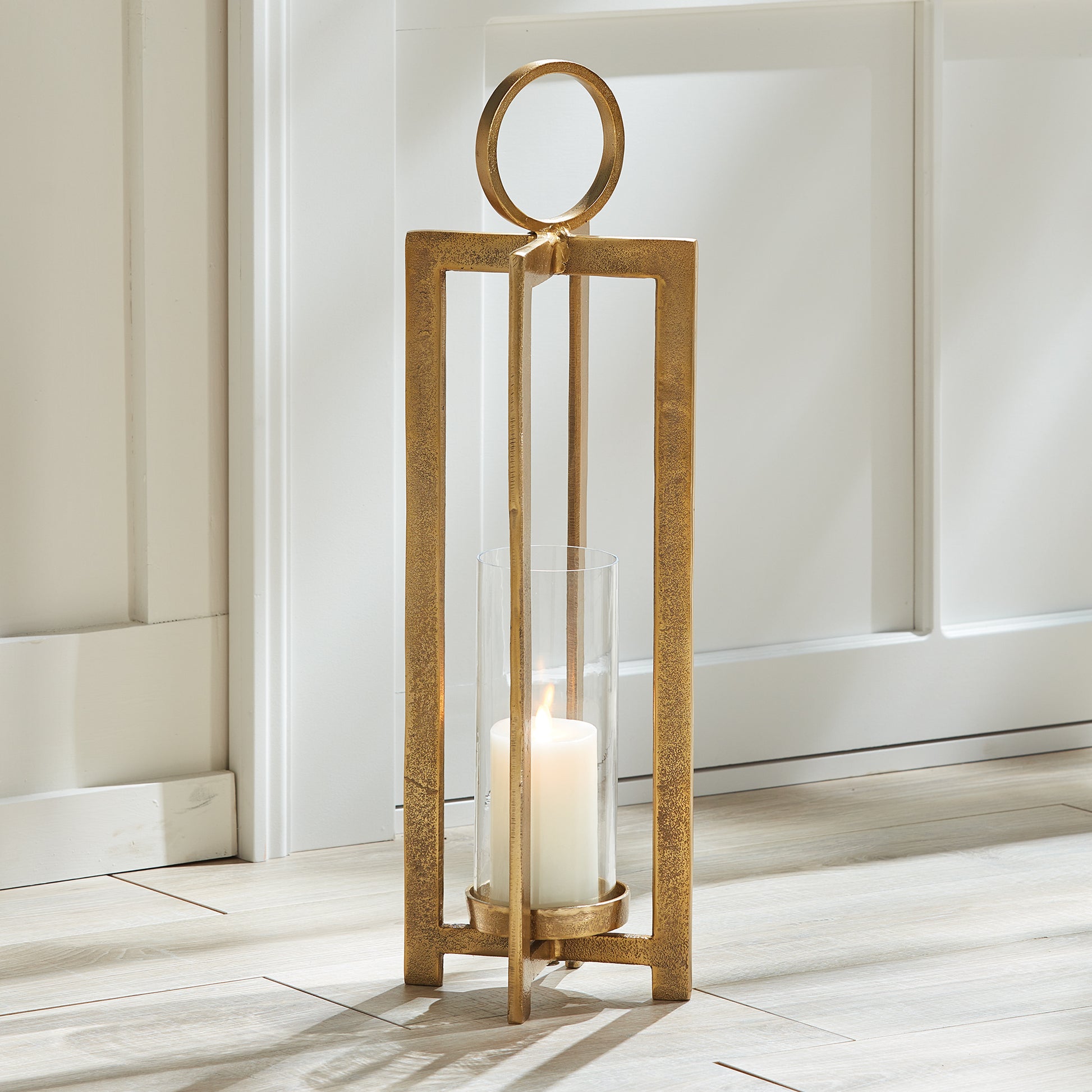 Elevate your space with the Asola Gold Hurricane Lantern Small. Exuding modern sophistication, this lantern boasts a striking form and impressive scale. With a footed detail that showcases your candle in style and a large round handle for effortless transportation, it's the perfect addition to mantles, front entries, and any other area in need of a touch of elegance.