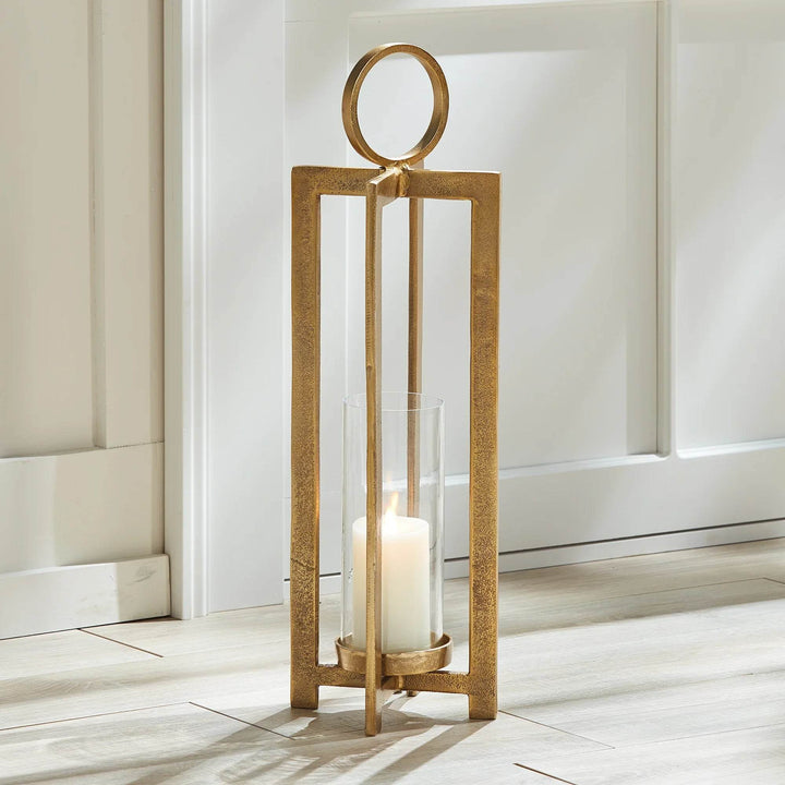 Elevate your space with the Asola Gold Hurricane Lantern Small. Exuding modern sophistication, this lantern boasts a striking form and impressive scale. With a footed detail that showcases your candle in style and a large round handle for effortless transportation, it's the perfect addition to mantles, front entries, and any other area in need of a touch of elegance.