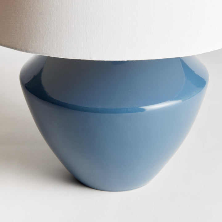 Crafted from a wooden mold dating back centuries, this stunning table lamp boasts a timeless silhouette and a deep blue finish. Topped with a tapered fabric shade, it adds a touch of history and elegance to any room, whether it be a family room, study, or bedroom. This ceramic blue table lamp is a dynamic addition to any space.