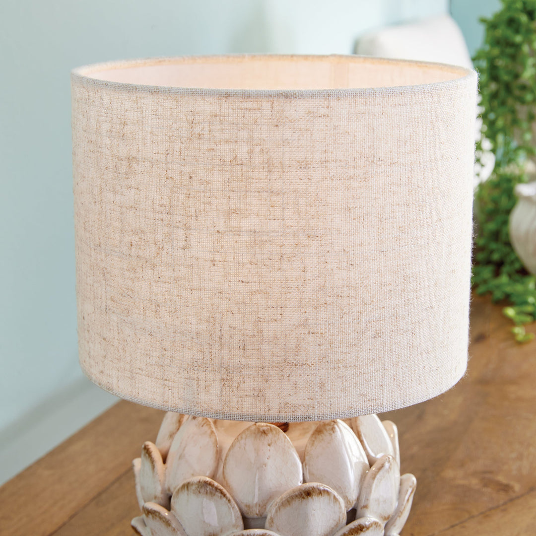 Transform your space with this exquisite ceramic table lamp, inspired by the intricate beauty of artichokes. Hand-finished with antique edges, it exudes a timeless elegance. Complete with a natural linen shade, this lamp is the perfect addition to any sophisticated and exclusive setting.