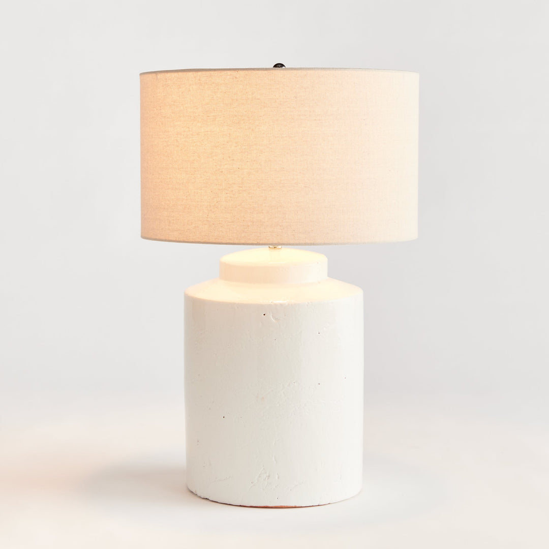 This Monty White Transitional Table Lamp is crafted from elegant white ceramic with a thick glaze, making it a perfect addition to transitional décor. Its generously-sized white linen shade and sleek finial add a touch of sophistication to its timeless design. The table lamp's construction is elegant and durable, creating a lasting beauty that will elevate any space. Add character and style to any room with this versatile and sophisticated lamp.