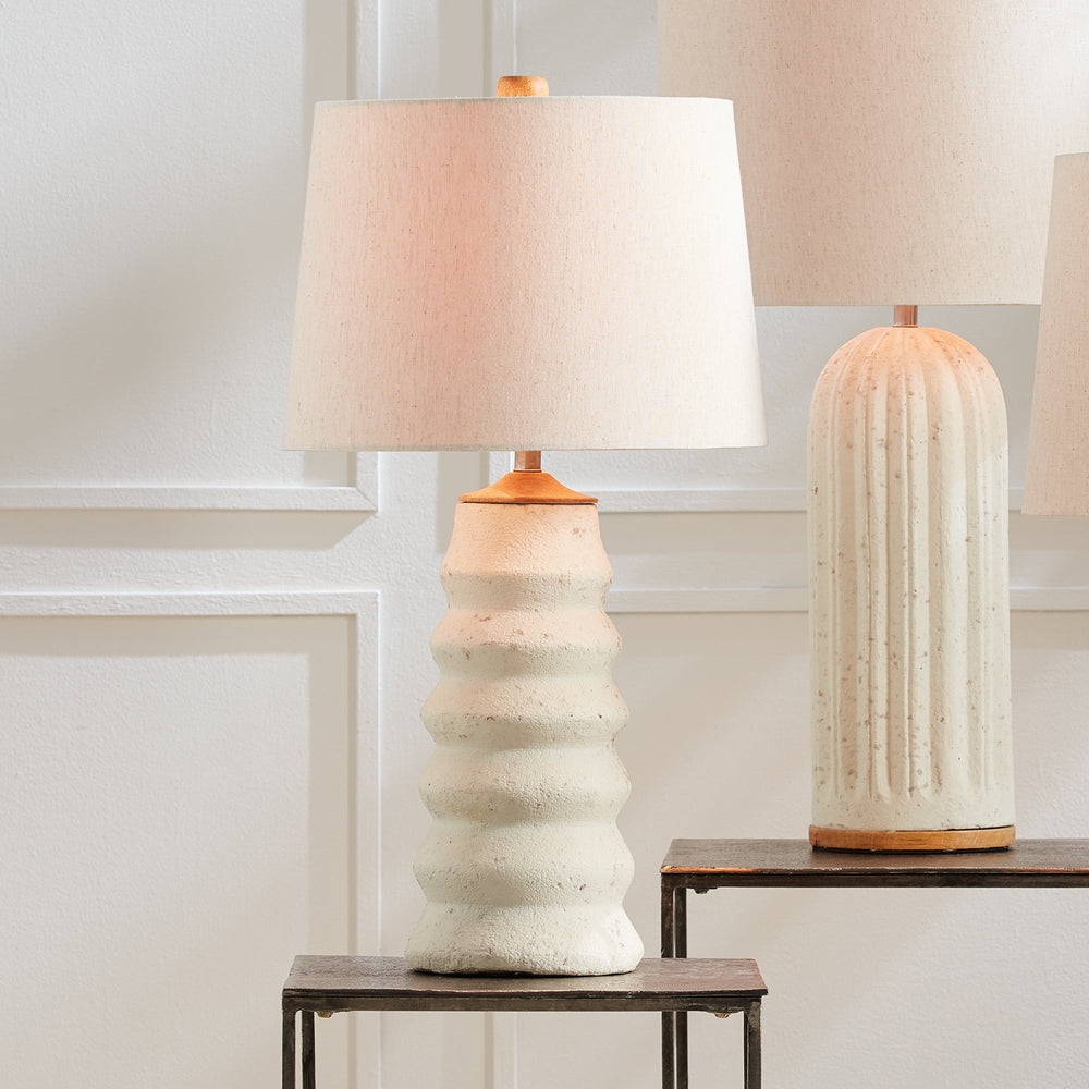 Enhance your living area with the Adria Table Lamp. This elegant table lamp features a natural cream eco-mix with a unique pitted texture, creating a lasting and warm white glow. The tapered shade adds a touch of sophistication to any living room.