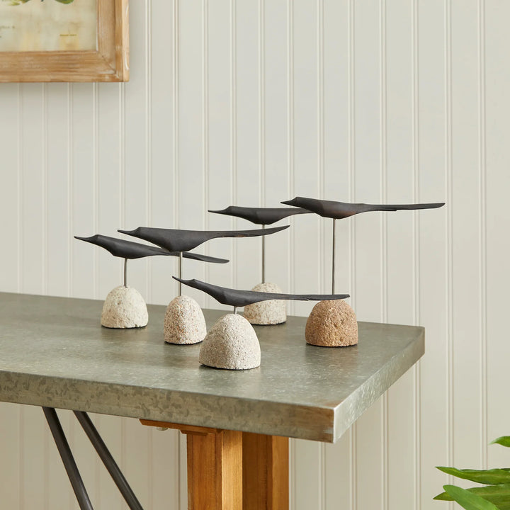 Decorative sculpture of black birds on stone bases on a table against a light-colored wall.