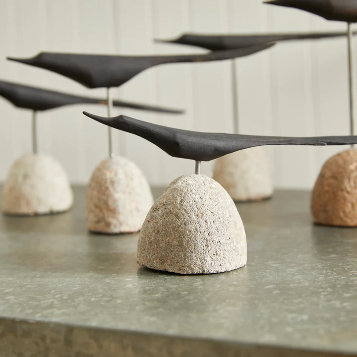 Black wooden birds balanced on textured white stones on a concrete surface.