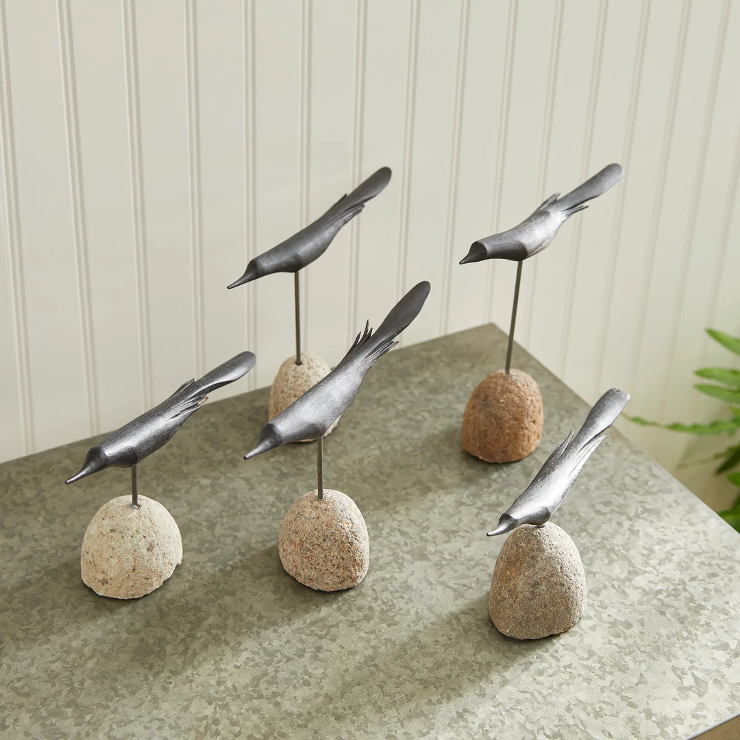 Decorative metal birds on stone bases on a table with a neutral background