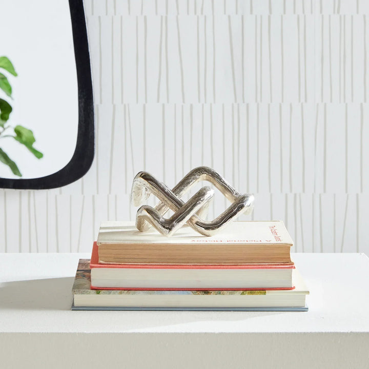 Decorative metal sculpture on a stack of books with a white textured wall background