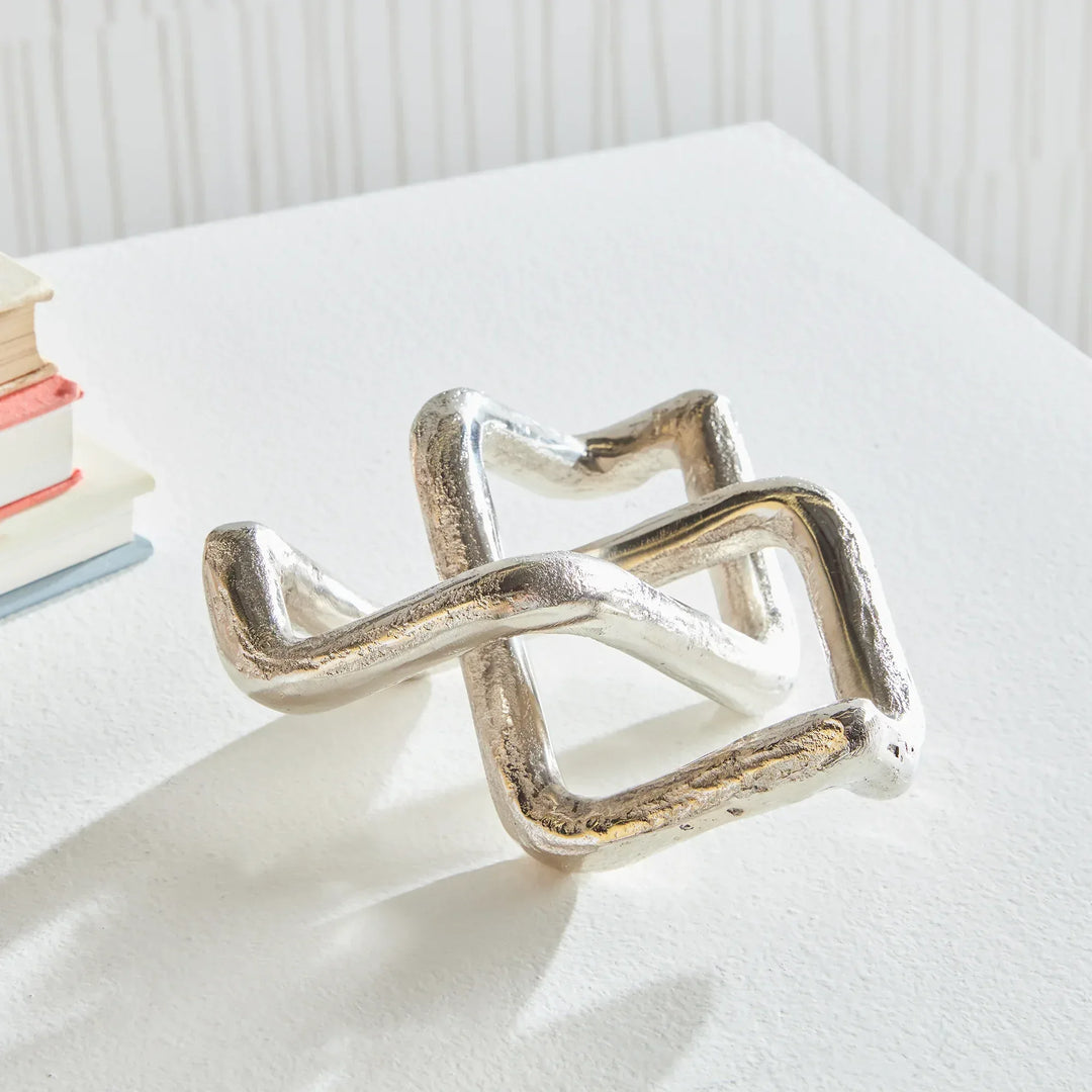 Silver geometric ring on a white surface with books in the background