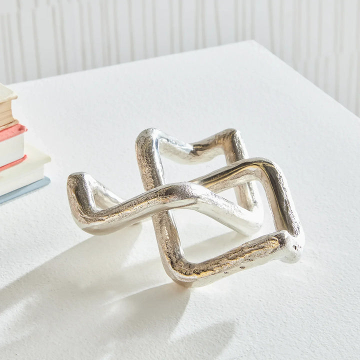 Silver geometric ring on a white surface with books in the background