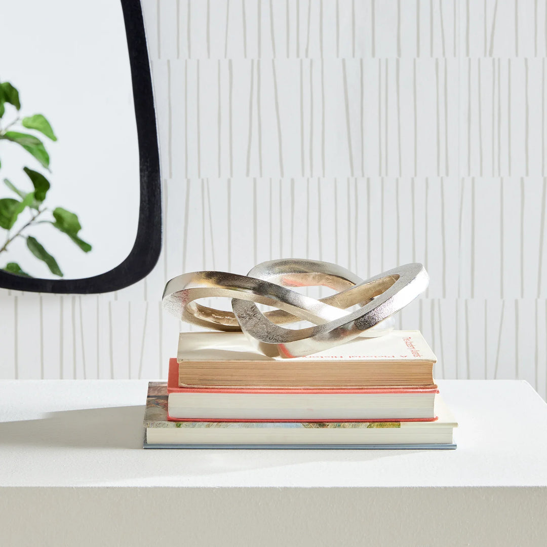 Decorative metal sculpture on a stack of books with a white textured wall background