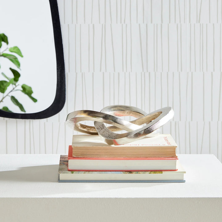 Decorative metal sculpture on a stack of books with a white textured wall background