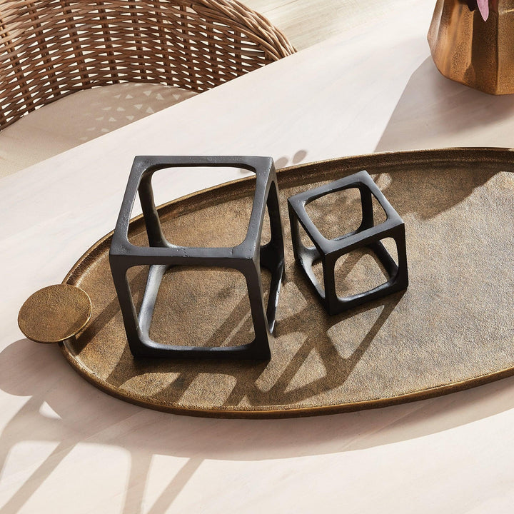 Decorative black cube sculptures on a textured surface with wicker basket and wooden object in the background