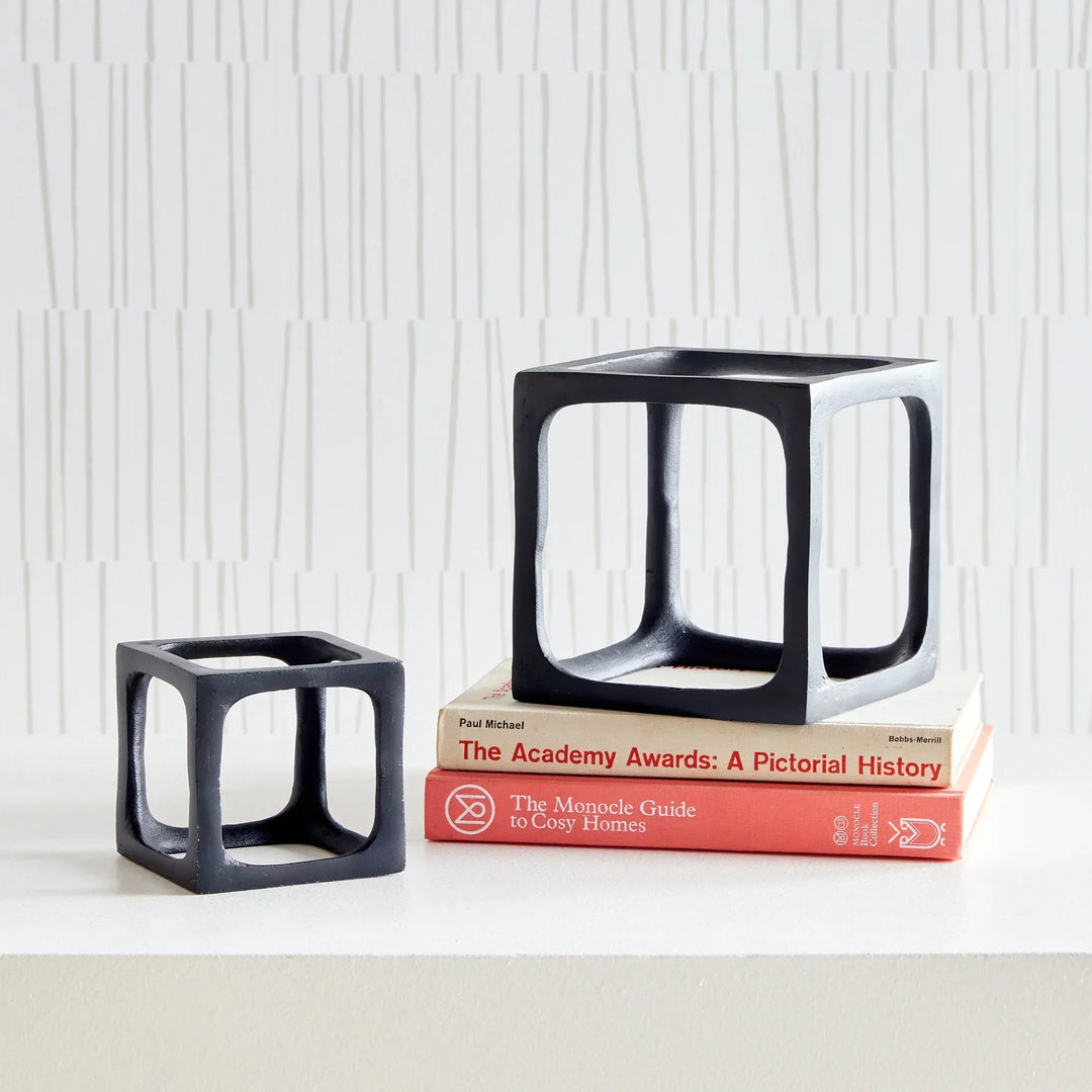 Two black cube-shaped sculptures on a white surface with a textured white wall background