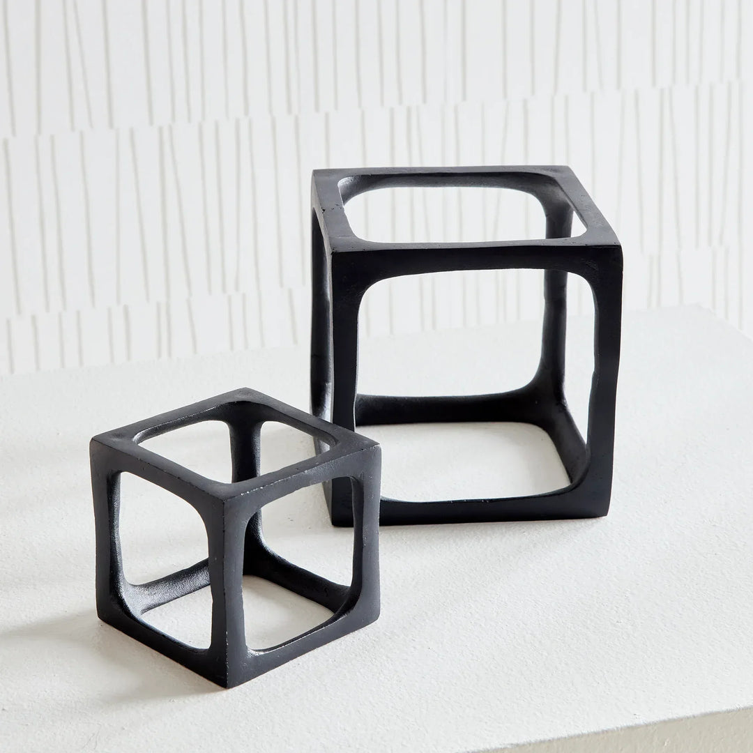 Two black geometric cube tables on a white surface with a white textured wall background