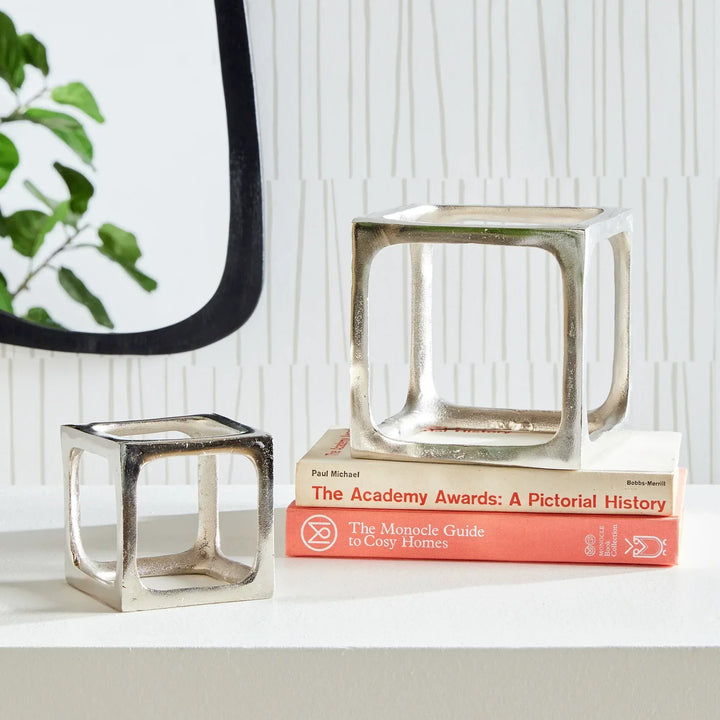 Decorative silver cube sculpture on a stack of books with a plant in the corner