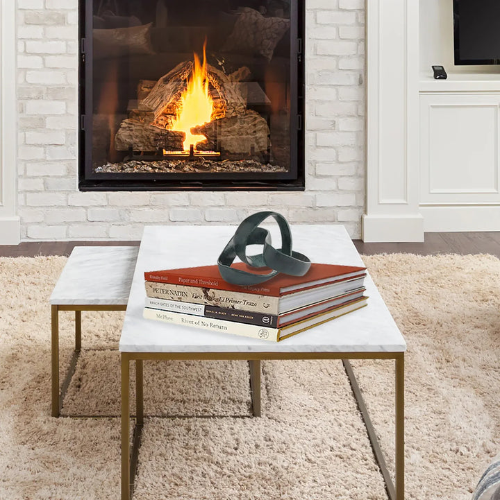 Coffee table with books and sculpture in front of a fireplace.