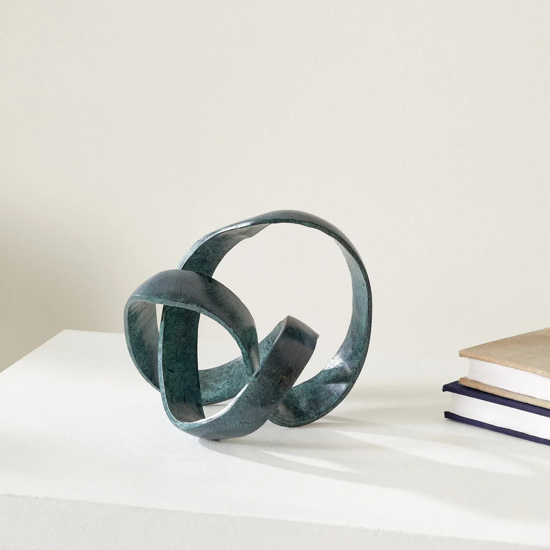 Abstract metal sculpture on a white surface with a light gray background