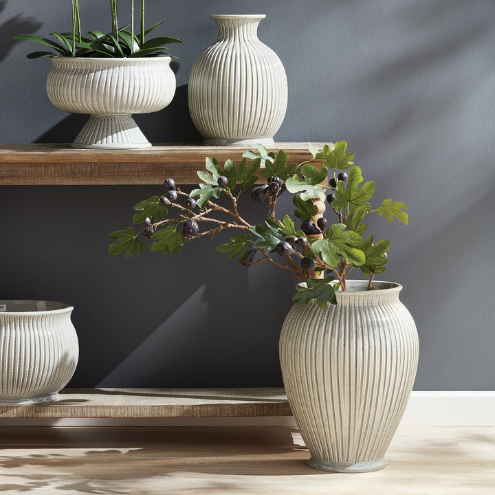 Decorative vases and plants on a wooden shelf against a dark wall.