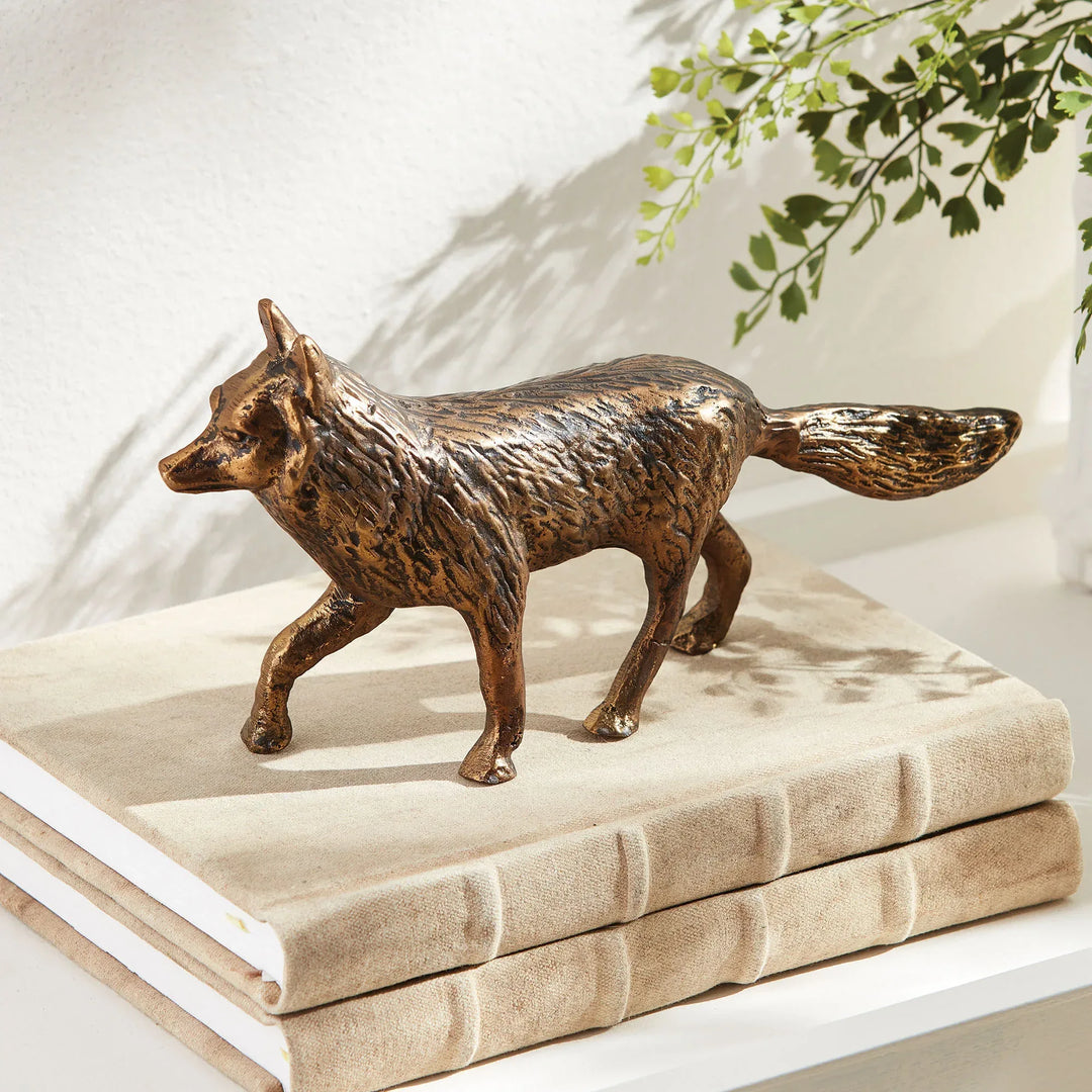Bronze fox figurine on a stack of books with a plant in the background