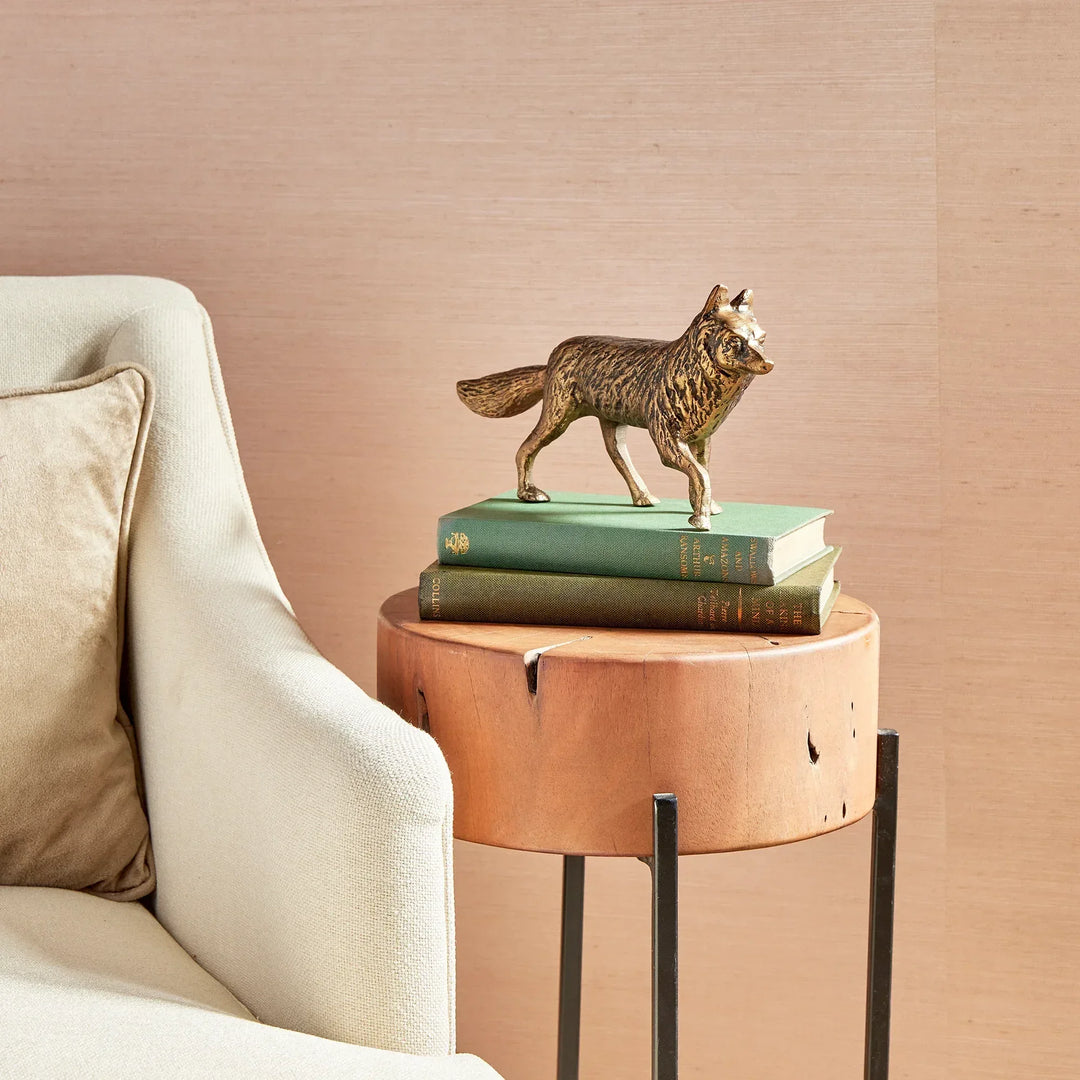 Wooden side table with a wolf figurine and books next to a beige armchair.