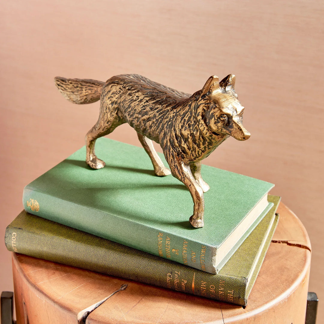 Bronze wolf figurine on top of green books with a beige background