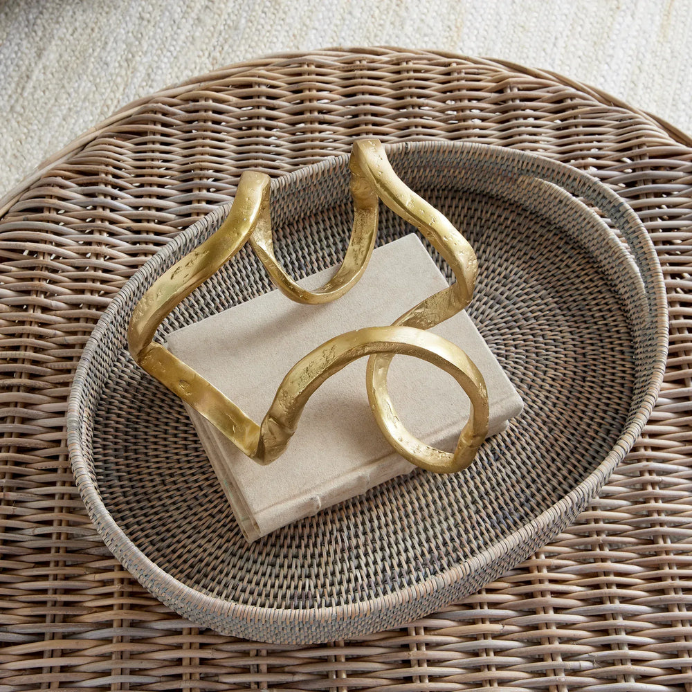 Decorative gold sculpture on a stack of white napkins with a wicker tray underneath.