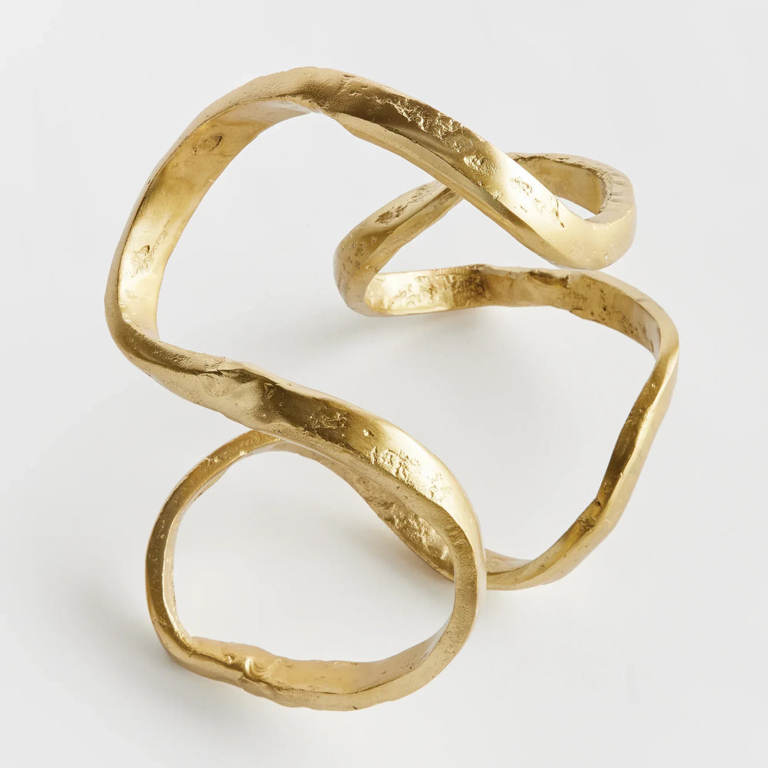 Gold sculpture with a twisted design on a light gray background