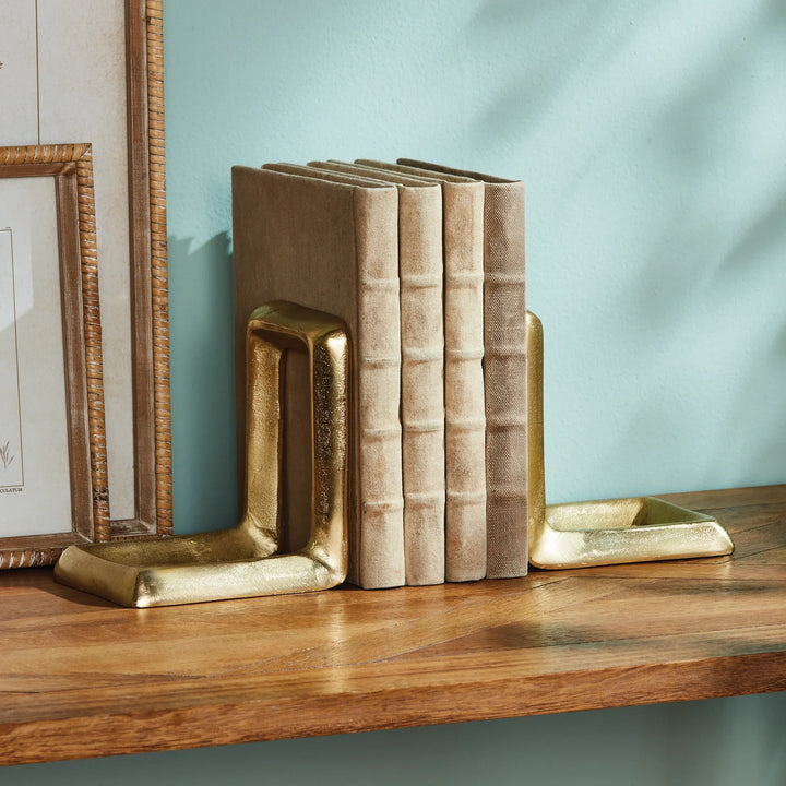 Gold bookends and decorative books on a wooden shelf against a light blue wall.