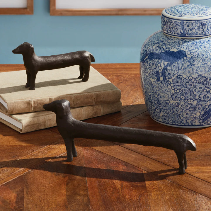 Two bronze dog-shaped objects on a wooden surface with a blue and white ceramic jar in the background.