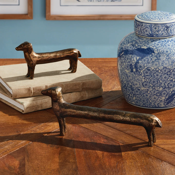 Bronze dog figurines on a wooden surface with a blue floral-patterned jar in the background.