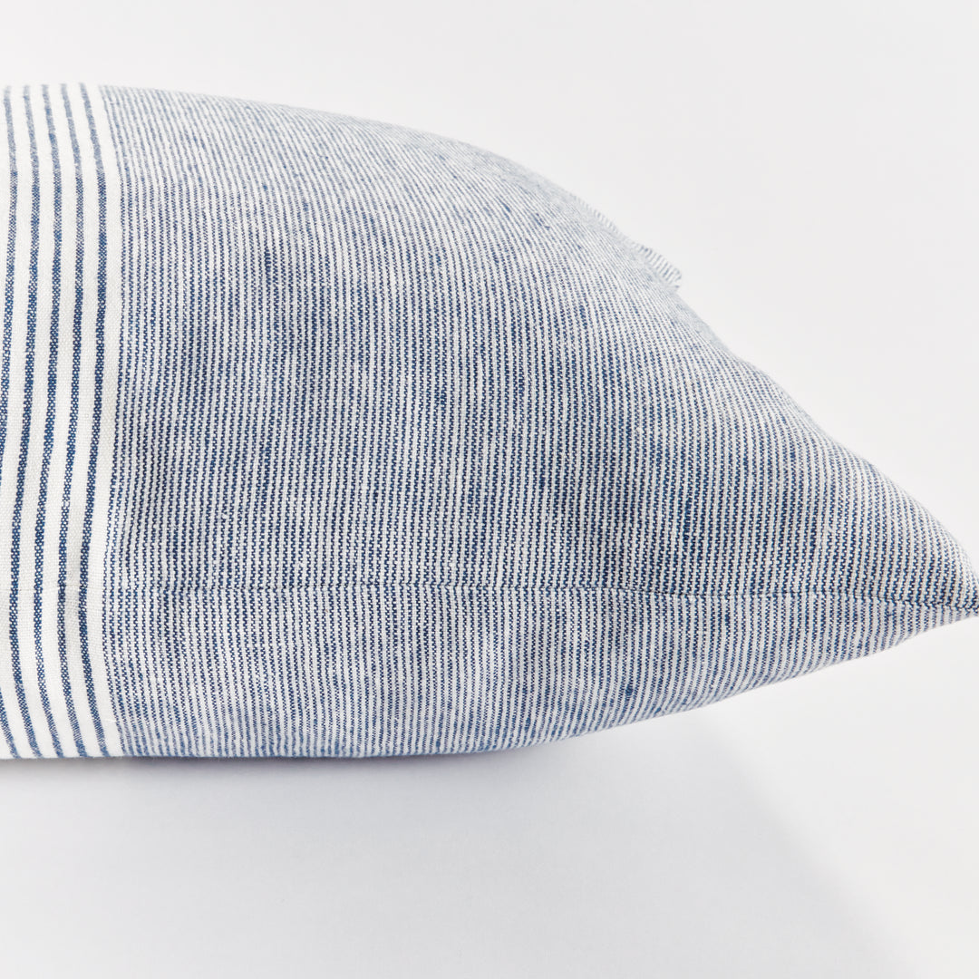 Navy and ivory linen pillow next to a seated figure in neutral clothing, minimalist coastal room


