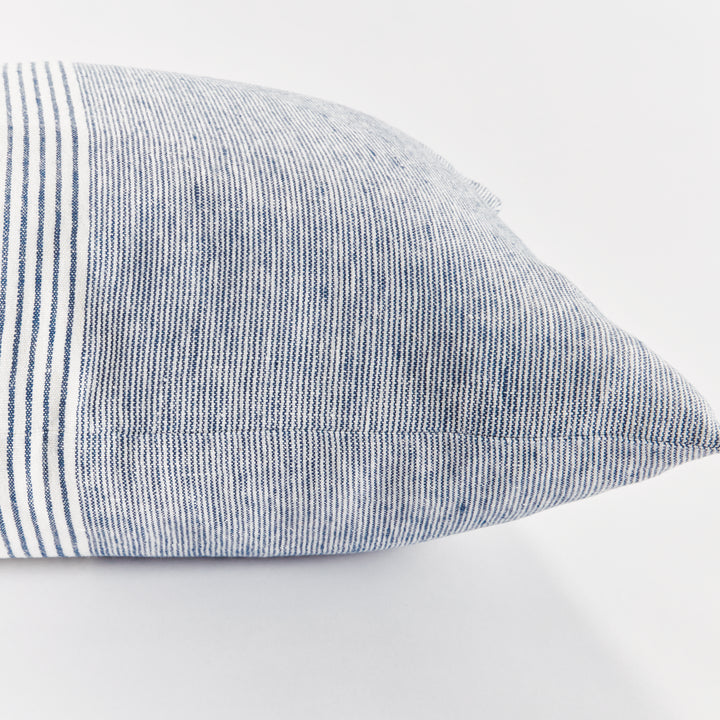 Navy and ivory linen pillow next to a seated figure in neutral clothing, minimalist coastal room


