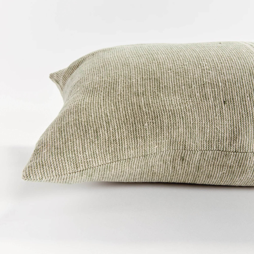 Green and flax pinstripe lumbar pillow layered with neutral cushions on a light linen sofa, evoking a relaxed, sunwashed coastal living room.

