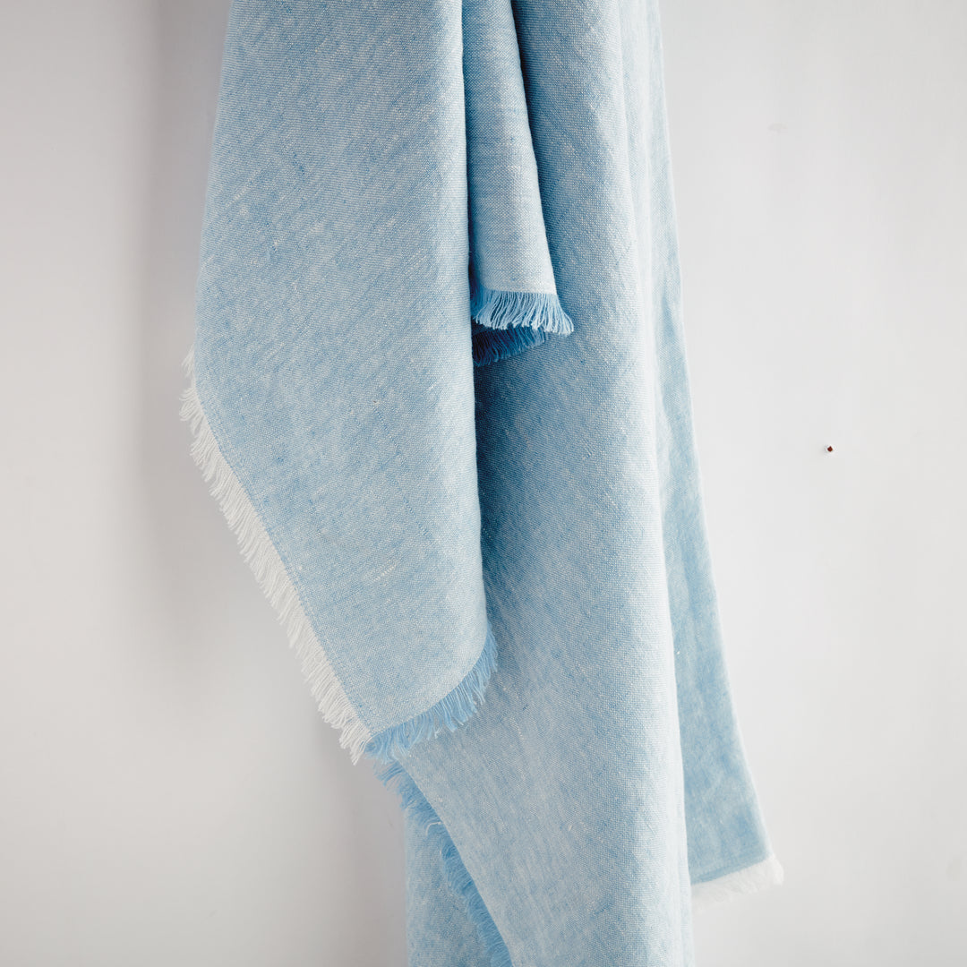 Detailed texture view of pre-washed European flax linen in soft blue, revealing the quality weave and frayed edging.