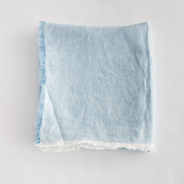 Light blue linen throw draped over a cream-toned coastal sofa, styled in a serene, beach-inspired interior