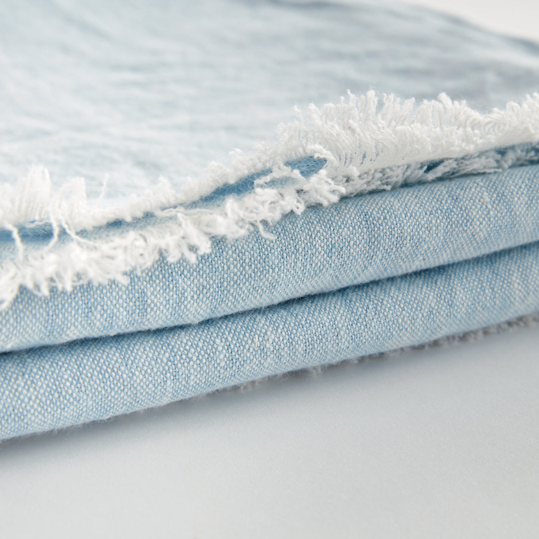 Close-up of light blue flax linen throw blanket folded neatly, highlighting the fine weave and coastal-inspired color