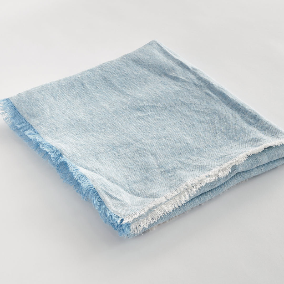 Angled view of light blue European linen throw showing soft frayed edge and layered fabric, ideal for home styling.