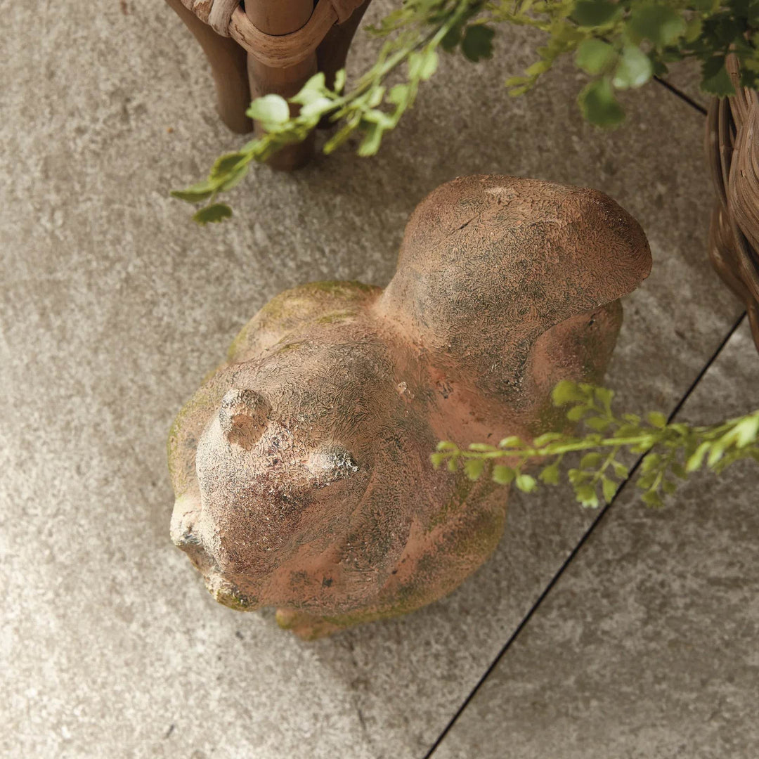 Decorative squirrel statue in moss terracotta finish, styled on patio tile with visible aged and pitted texture.

