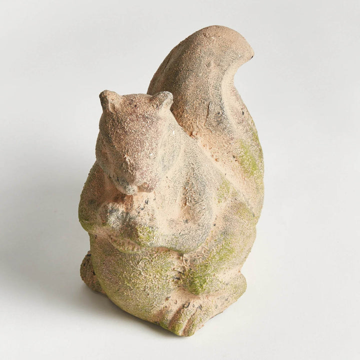 Top-down angle of moss terracotta squirrel sculpture, showing its seated form, large tail, and natural stone-like texture.

