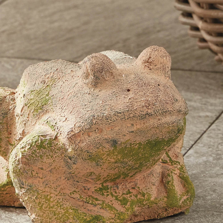 Handcrafted moss terracotta frog sculpture with textured patina, viewed at an angle to show curved body and folk-art form.

