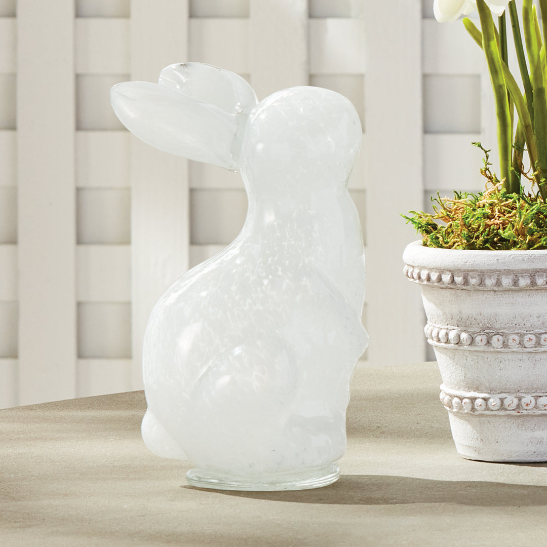 White textured rabbit sculpture on a surface with a plant in the background